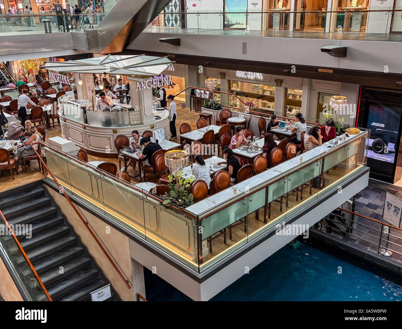 Blick auf das Angelina Café im Einkaufszentrum Marina Bay Sands in Singapur. Die Tische sind von Gästen besetzt und das Café ist voll. Stockfoto