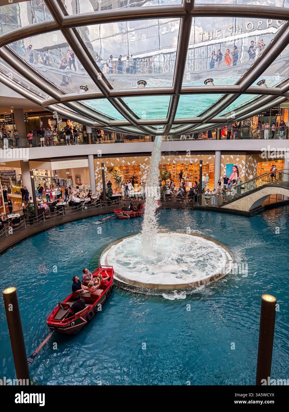 Marina Bay Sands Einkaufszentrum. Besucher machen eine Sampanfahrt um den Rain Oculus. Luxusgeschäfte sind im Hintergrund zu sehen. Stockfoto