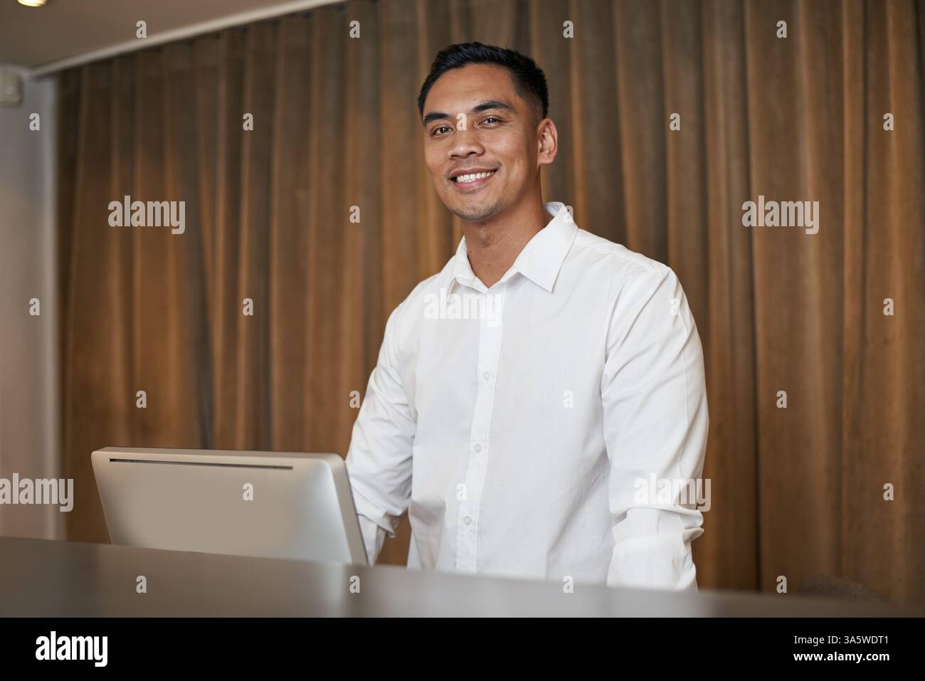 Smiling Hotel Professional in weißem Hemd am Computer in modernem Interieur Stockfoto