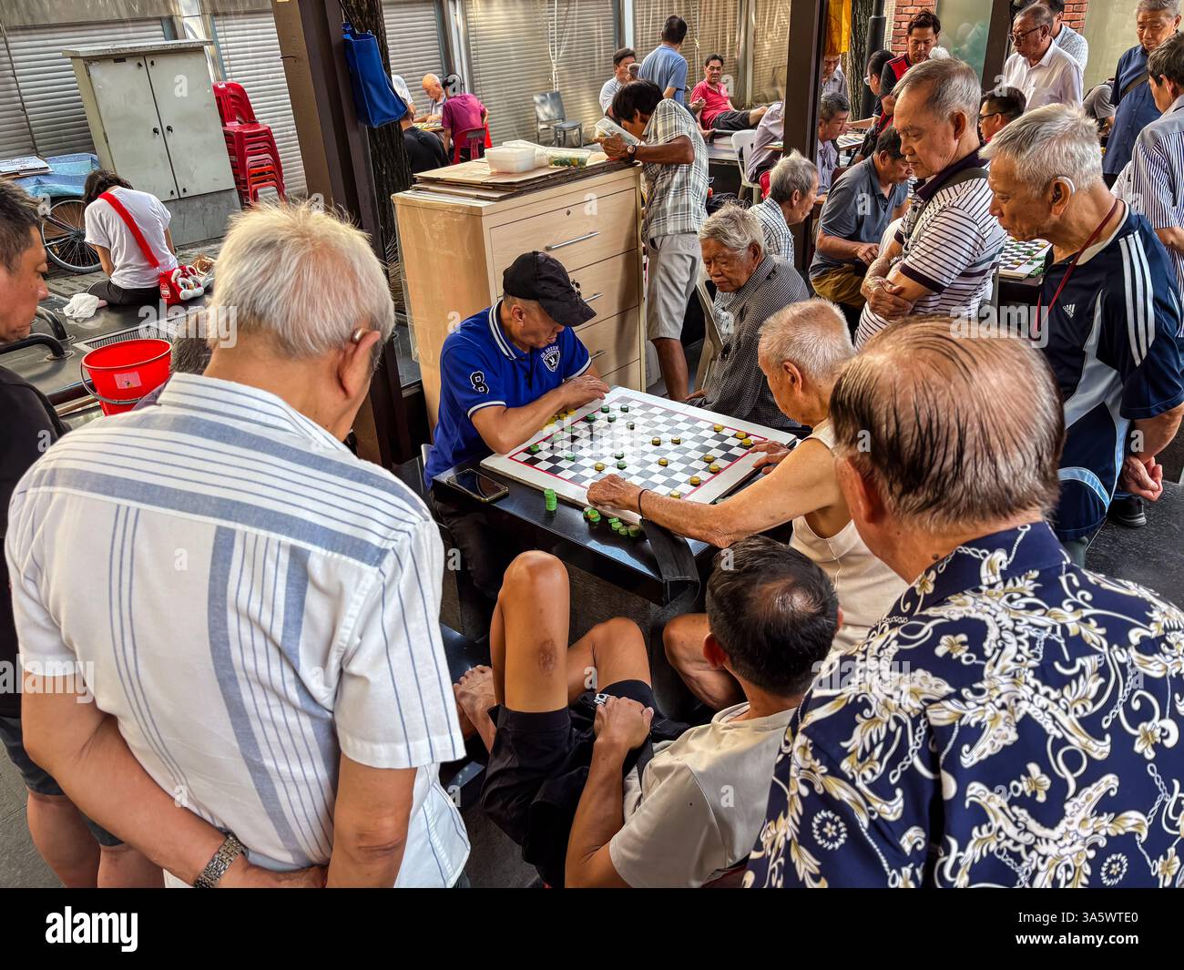 Ältere Männer spielen chinesische Checkers in Singapur. Die Spieler und Zuschauer konzentrieren sich auf das Spiel. Stockfoto