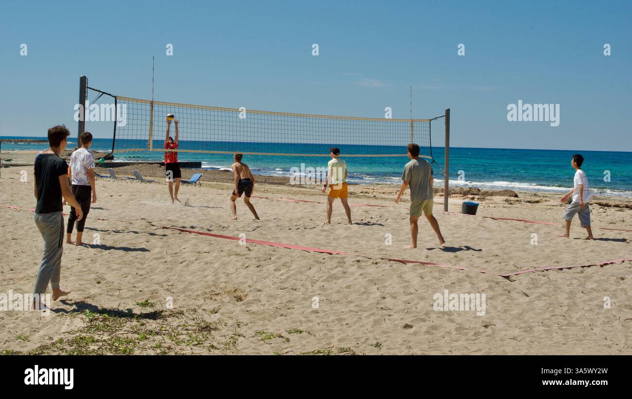 Eine Gruppe junger Freunde spielt ein spannendes Volleyballspiel an einem Sandstrand mit einem lebhaften Meereshintergrund unter freiem Himmel Stockfoto