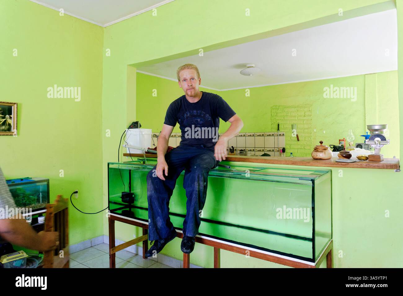 Der Mann, der das Aquarium und den Palisander-Ständer gebaut hat, beweist, wie robust beide sind, indem er am Rand des Tanks sitzt, in Jinotega, Nicaragua. S Stockfoto