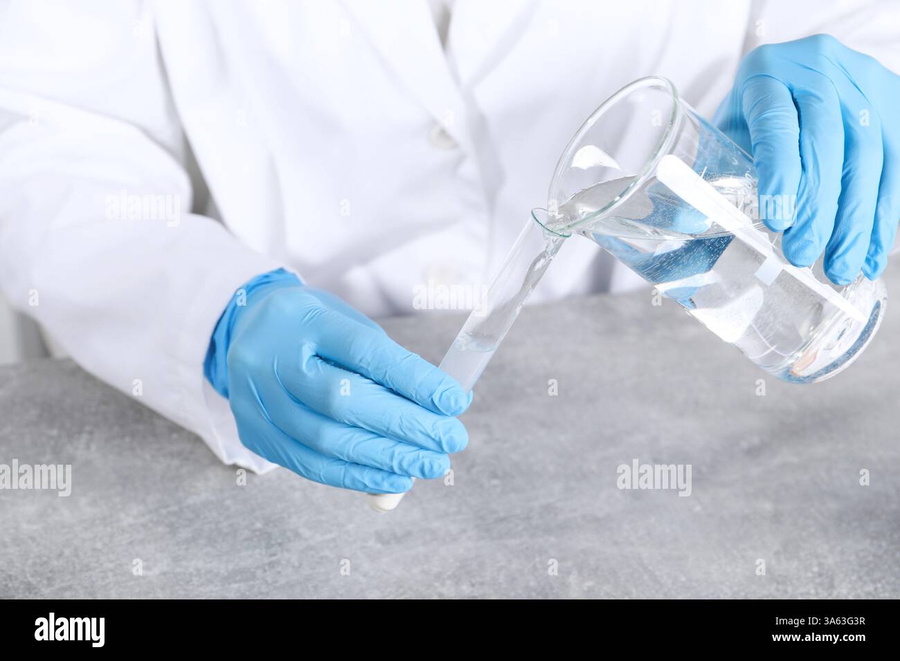 Labortests. Wissenschaftler gießen Flüssigkeit in das Reagenzglas am grauen Tisch drinnen, Nahaufnahme Stockfoto