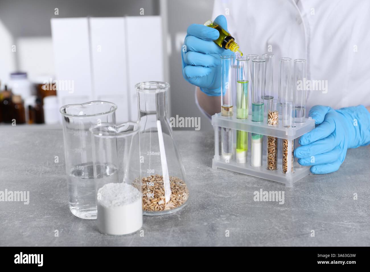 Labortests. Wissenschaftler tropft Flüssigkeit in Reagenzglas am Tisch drinnen, Nahaufnahme Stockfoto