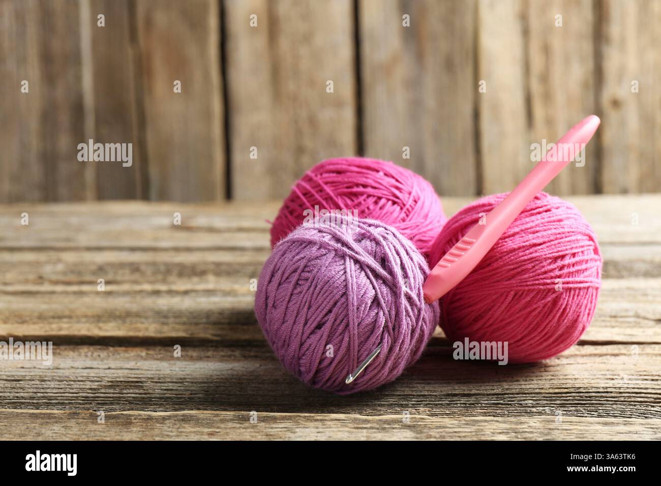 Kugeln aus buntem Garn und Häkelnadel auf Holztisch, Nahaufnahme. Leerzeichen für Text Stockfoto