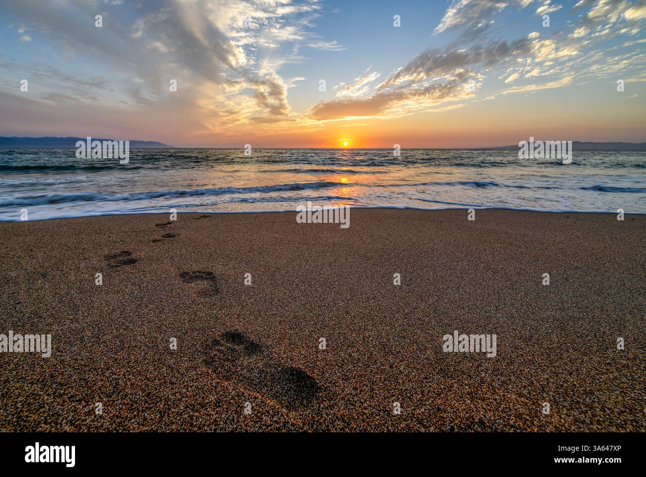 Fußspuren im Sand, die zum Sonnenaufgang des Ozeans führen Stockfoto
