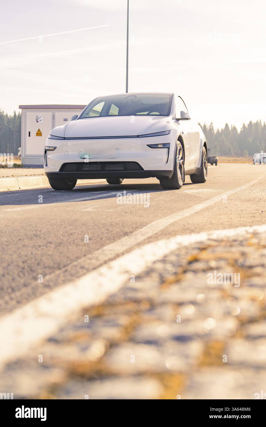Weißes modernes Auto auf der Straße im Hintergrund mit Wald und Sonnenschein, Tesla, neues Model Y Juniper, Deutschland, Europa Stockfoto