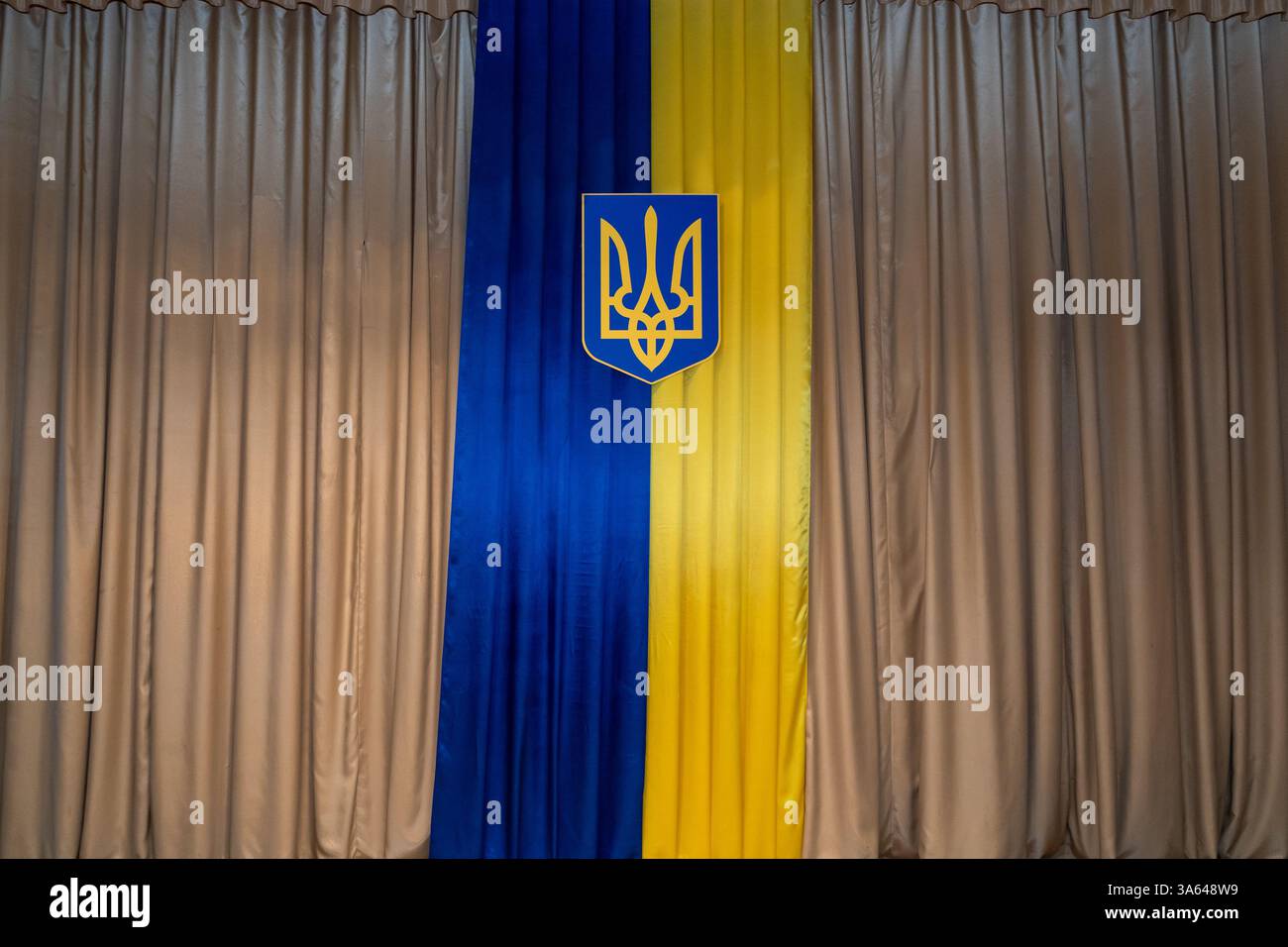 Eine große ukrainische Flagge mit blauen und gelben Farben hängt in einem formellen Saal. Das Wappen ist als Teil der patriotischen Dekoration mittig ausgerichtet Stockfoto