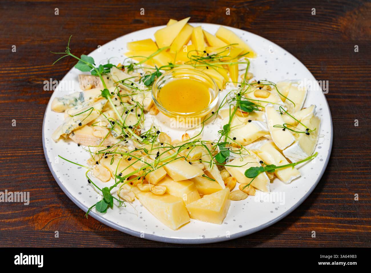 Eine wunderschön gestaltete Platte mit verschiedenen Käsesorten, frischem Obst und Honig. Das Gericht wird in einem schicken Restaurant serviert, perfekt zum Teilen oder zum Essen Stockfoto