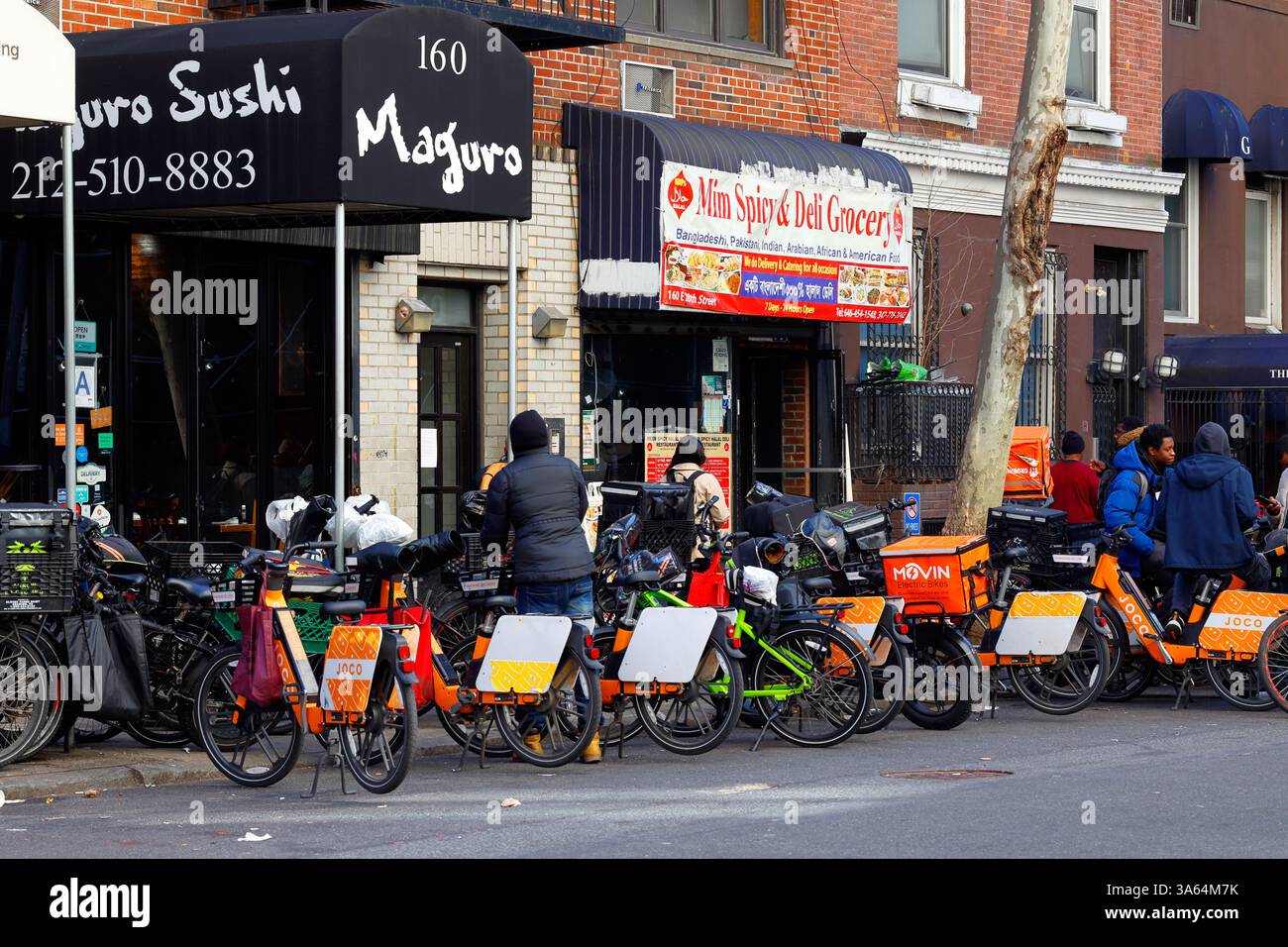 Gastronomiebetriebe und Joco-Verleih-E-Bikes, Elektrofahrräder vor einem kleinen Halal-Deli und Supermarkt in Manhattan, New York City Stockfoto