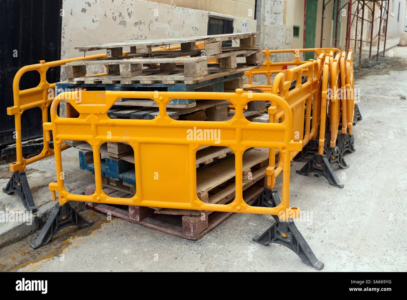 Hellorangefarbene Baubarrieren aus Kunststoff, die in der Nähe von Holzpaletten auf einer städtischen Straße gestapelt sind. Sicherheitsausrüstung für Baustellen, Baustellen Stockfoto