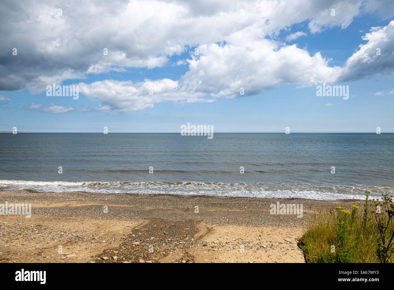 Kiesel- und Sandstrand in Skipsea, wo die Nordsee auf einen blauen, bewölkten Himmel trifft. UK Stockfoto
