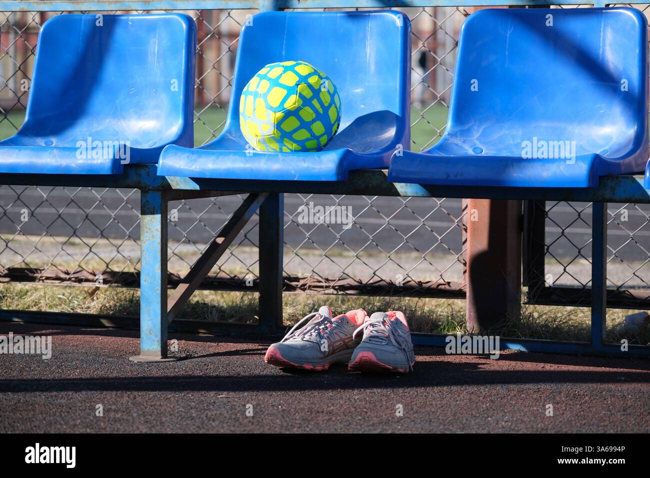 Ein Fußballball und Turnschuhe im Straßenstadion. Sie benutzten Schuhe, die nach dem Training unter der Ersatzbank platziert wurden. Sport unter freiem Himmel Stockfoto
