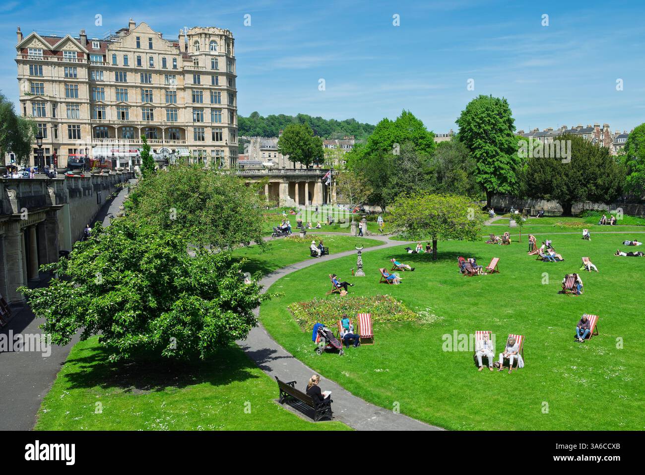 Leute, die warmes Wetter genießen, sitzen in Parade Gardens, Bath, Großbritannien. Der Park ist eine beliebte Touristenattraktion, ein Wahrzeichen neben dem Fluss Avon Stockfoto