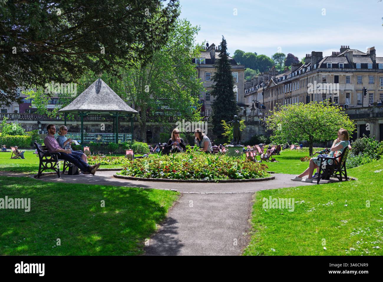 Leute, die warmes Wetter genießen, sitzen in Parade Gardens, Bath, Großbritannien. Der Park ist eine beliebte Touristenattraktion, ein Wahrzeichen neben dem Fluss Avon Stockfoto