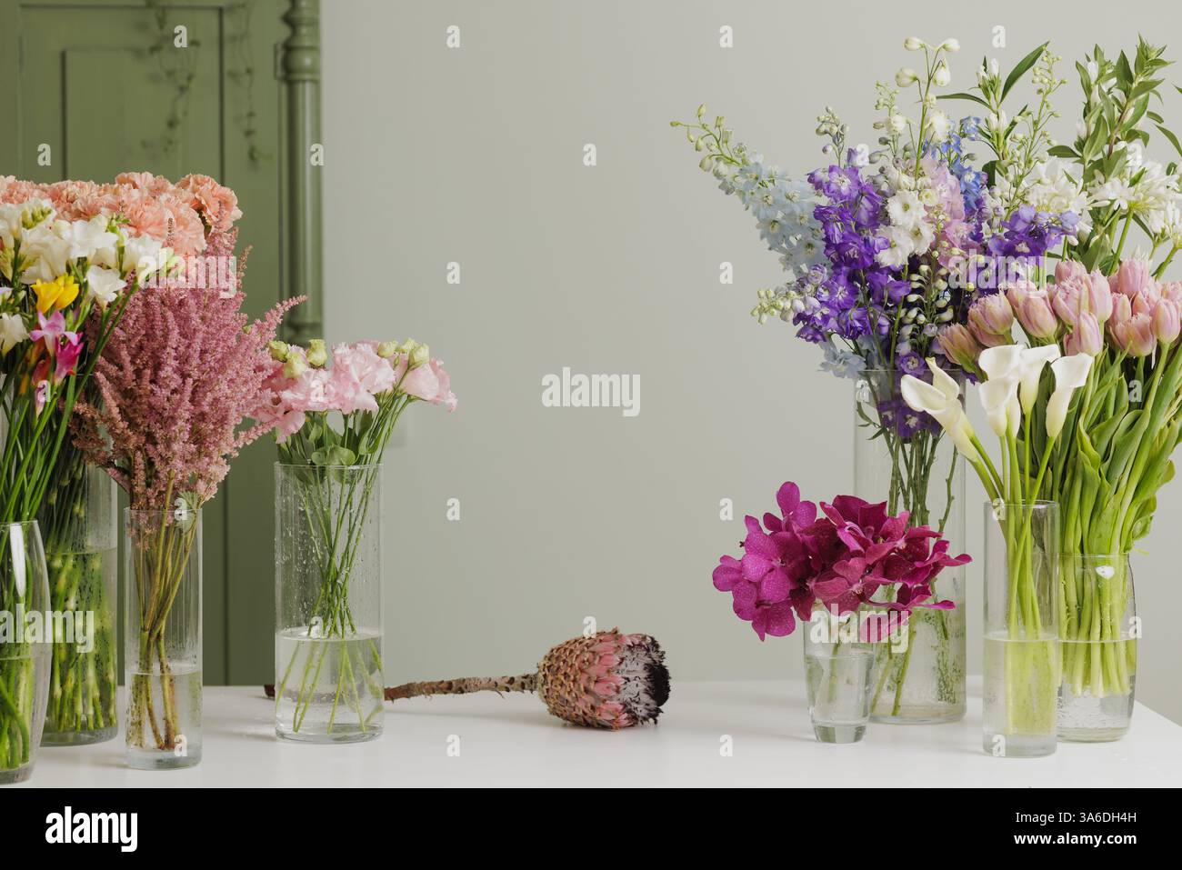 Elegantes Blumenarrangement mit frischen bunten Blumen in Glasvasen auf einem weißen Tisch vor einem weichen grünen Hintergrund, das eine ruhige Atmosphäre schafft. Stockfoto