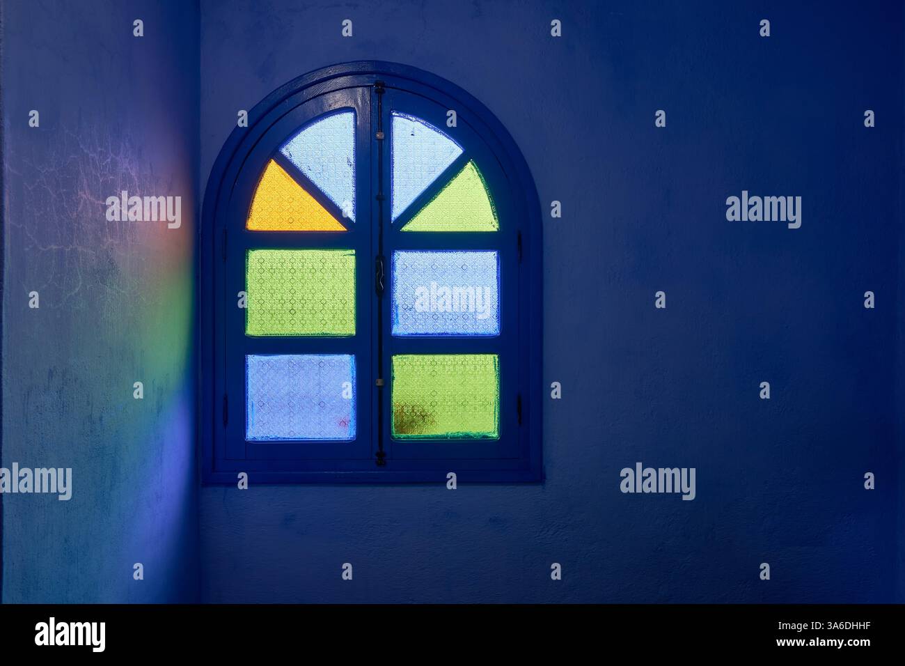 Innenansicht von Tageslicht durch grüne, blaue und gelbe Glasscheiben in einem geschlossenen bogenförmigen Holzfenster, Chefchaouen, Marokko Stockfoto