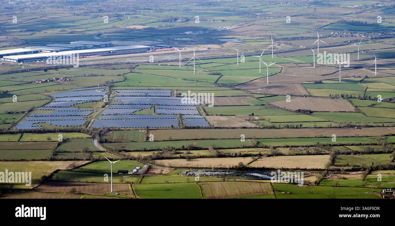 Ein Blick aus der Vogelperspektive auf große Distributionslager östlich von Rugby, West Midlands, UK, neben einer Stromquelle für einen Solarpark und Windturbinen Stockfoto