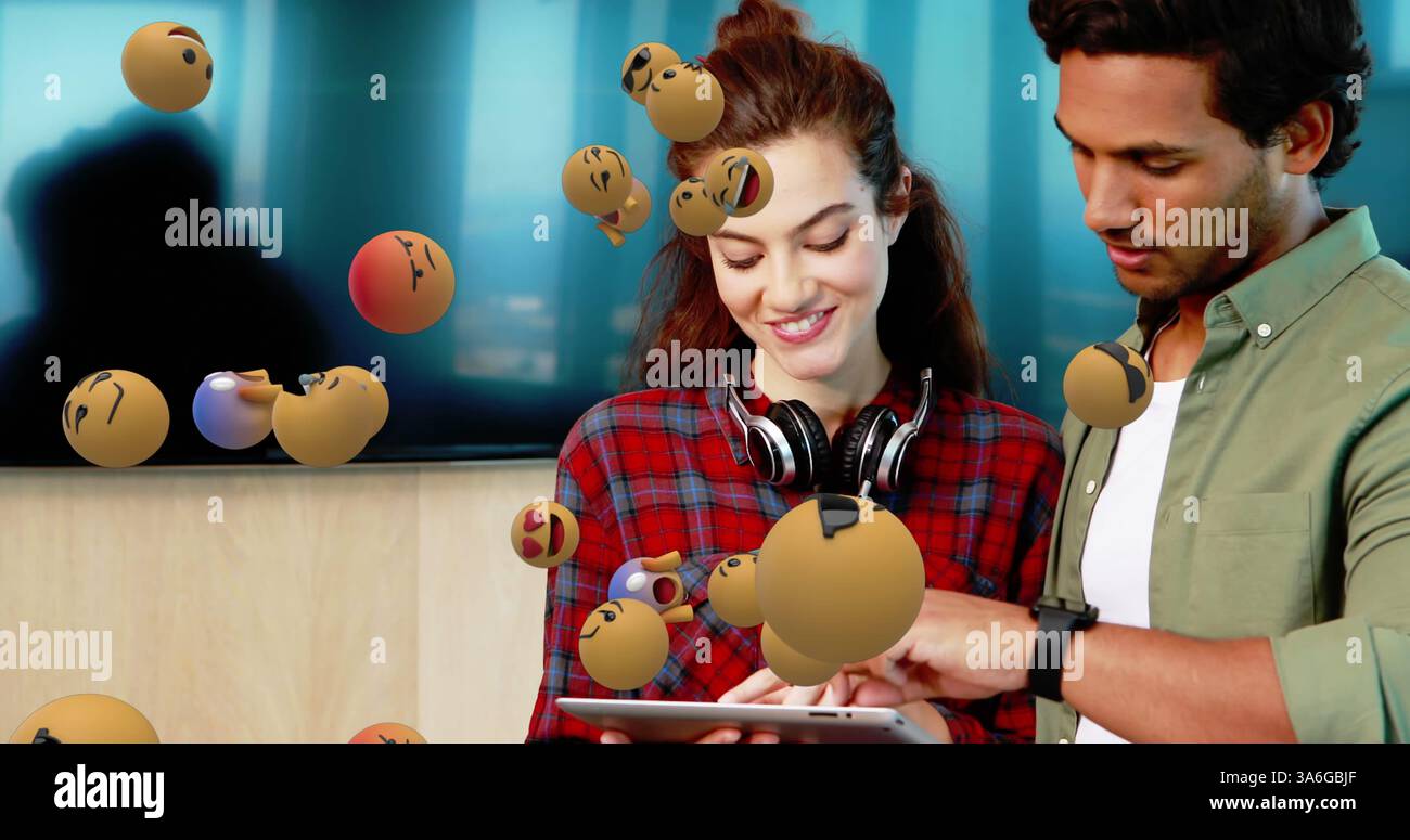Junge Profis, die in modernen Büros auf Tablets mit schwimmenden Emojis zusammenarbeiten. Teamwork, Zusammenarbeit, Technologie, digital, Innovation, Kommunikation Stockfoto