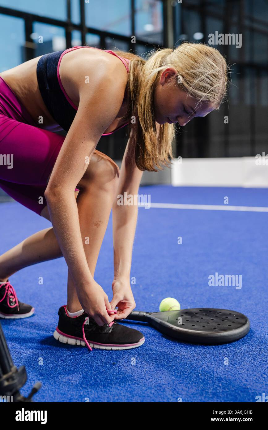 Frau, die Schnürsenkel auf dem Padel-Platz bindet, bereitet sich auf das Spiel mit Schlägern in der Nähe vor Stockfoto