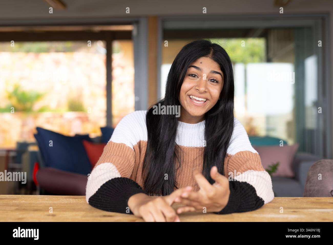 Lächelnder indischer Teenager zu Hause, der mit ausdrucksstarken Gesten Gespräche führt Stockfoto