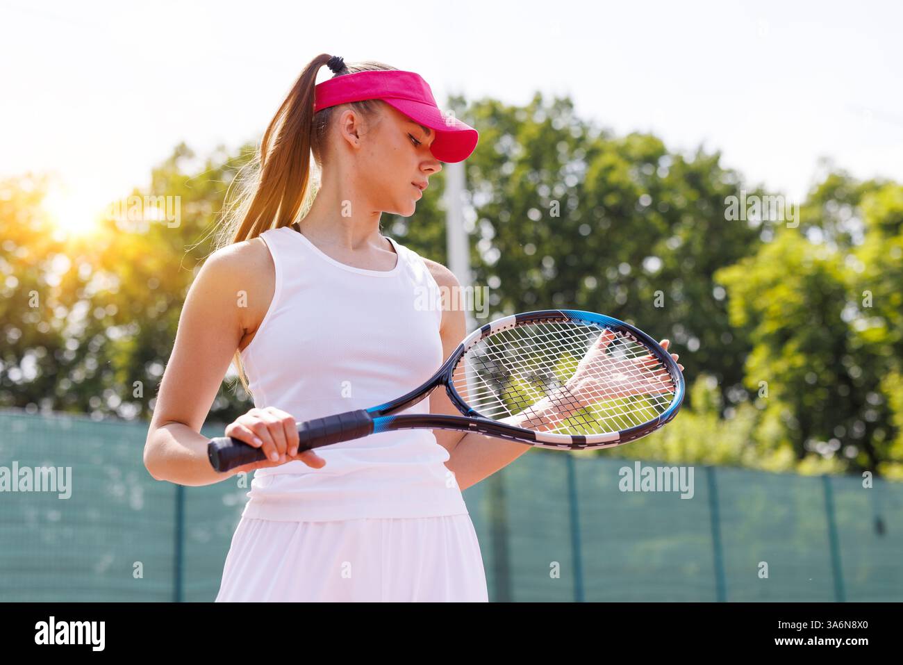 Weibliche Tennisspielerin, die Schläger auf dem Außenplatz inspiziert, konzentriert und bereit für das Spiel, Tennisspiel Stockfoto