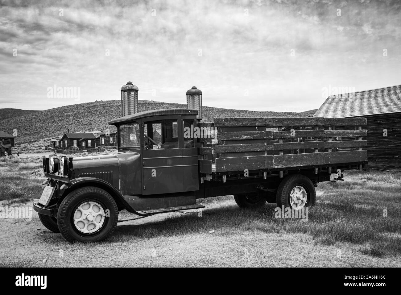 Ein alter alter Pritschenwagen, der neben zwei antiken Gaspumpen in Bodie Ghost Town geparkt hat. Schwarz-weiß. Stockfoto