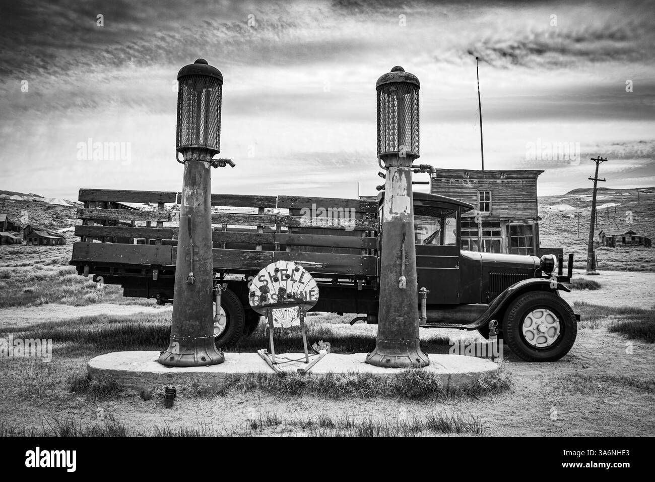 Ein alter alter Pritschenwagen, der neben zwei antiken Gaspumpen in Bodie Ghost Town geparkt hat. Schwarz-weiß. Stockfoto