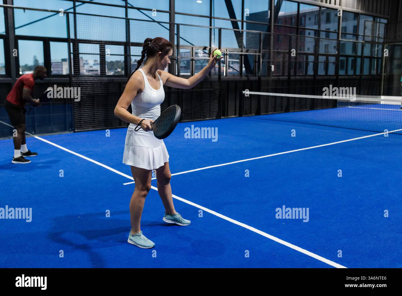 Frau in weißem Outfit spielt Padel-Tennis auf dem Hallenplatz, bereitet sich auf das Servieren vor, Kopierraum Stockfoto Frau in weißem Outfit spielt Padel-Tennis auf dem Hallenplatz, bereitet sich auf das Servieren vor, Kopierraum Stockfoto