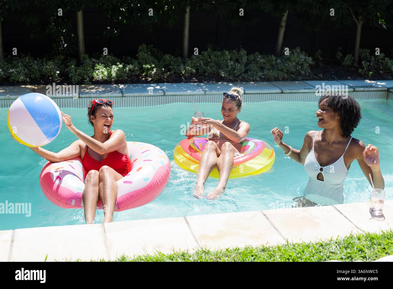 Verschiedene Freundinnen genießen Poolparty, lachen und spielen mit Strandball auf Wagen Stockfoto