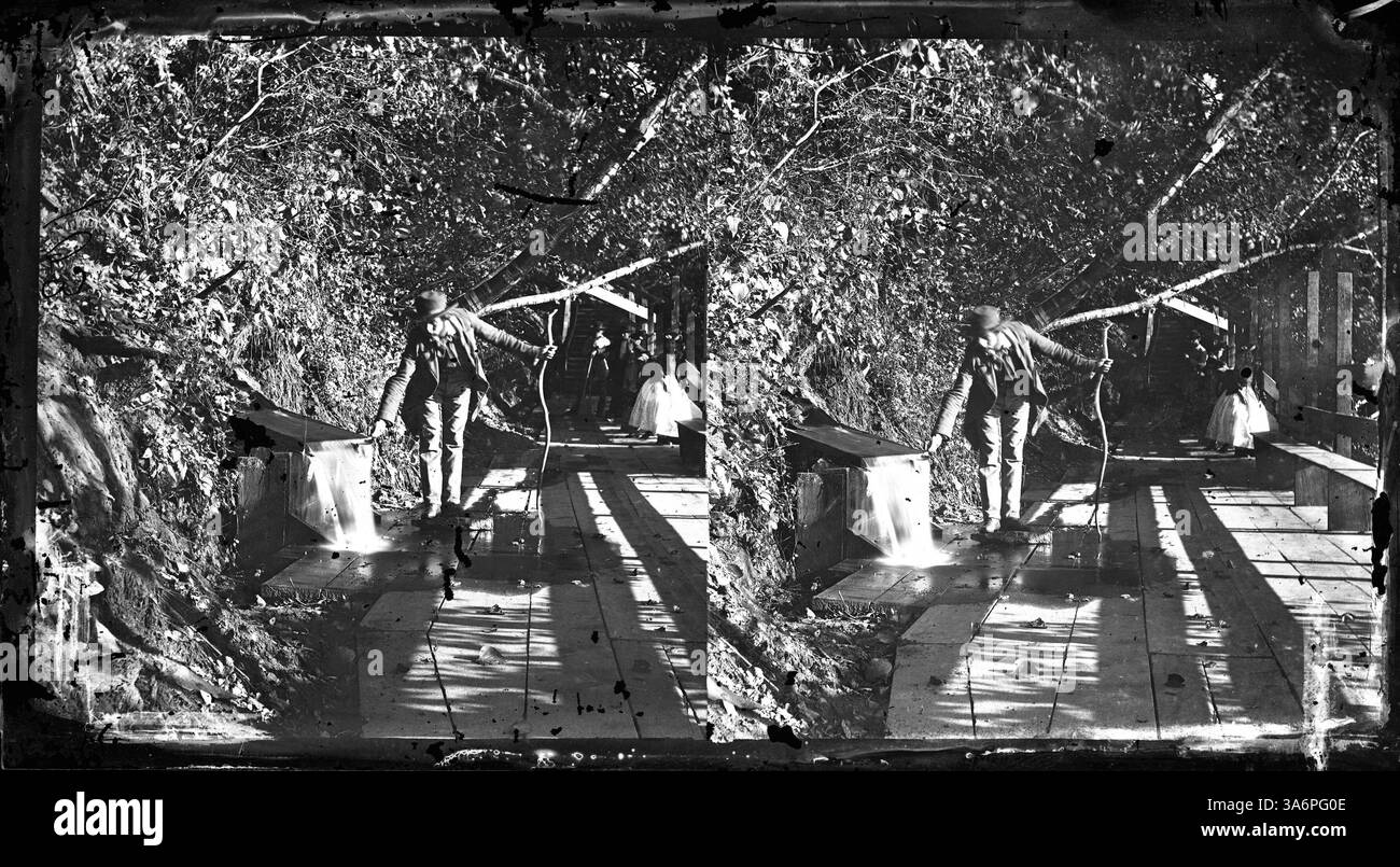 Pettingills Chalybeate Springs, die sich unter der St. Anthony-Seite der heutigen 10th Avenue Bridge befinden, waren in den frühen 1900er Jahren ein beliebter Ort für Besucher, um mineralreiches Wasser zu sammeln Ein Mann wird gesehen, wie er einen Topf mit Wasser auf einem Holzsteg füllt. Stockfoto