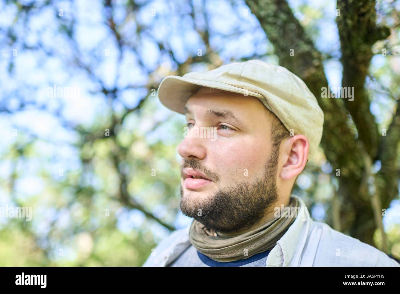 Porträt eines jungen Mannes im Freien, der zur Seite schaut, im Hintergrund sind Baumzweige, Kopierraum. Stockfoto