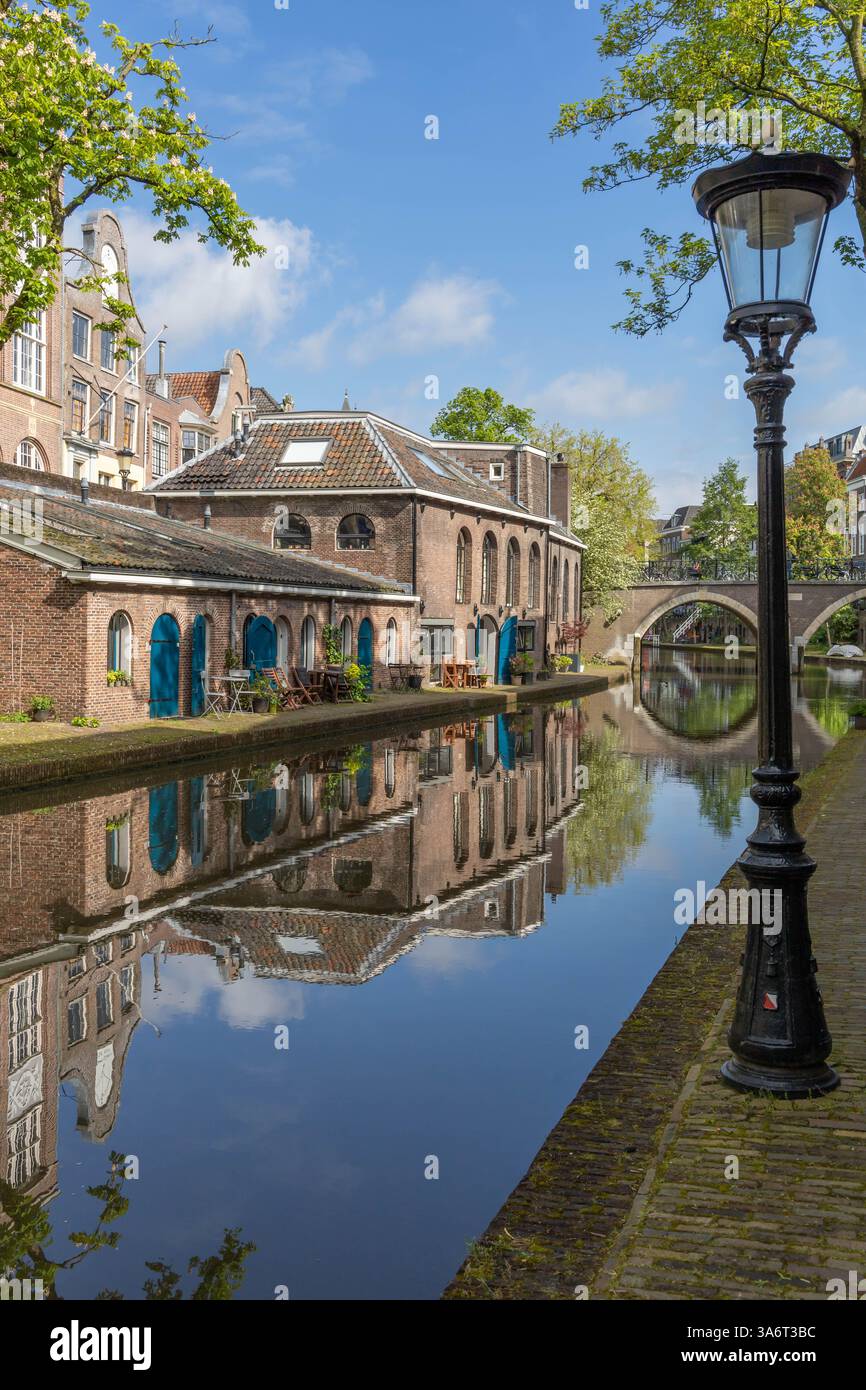 Oudegracht mit Ziegelhäusern in der Nähe des Kanals. Eine Brücke mit Fahrrädern, die an den Brücken befestigt sind, die sich im Kanalwasser spiegeln, eine eiserne Laterne auf dem Stockfoto