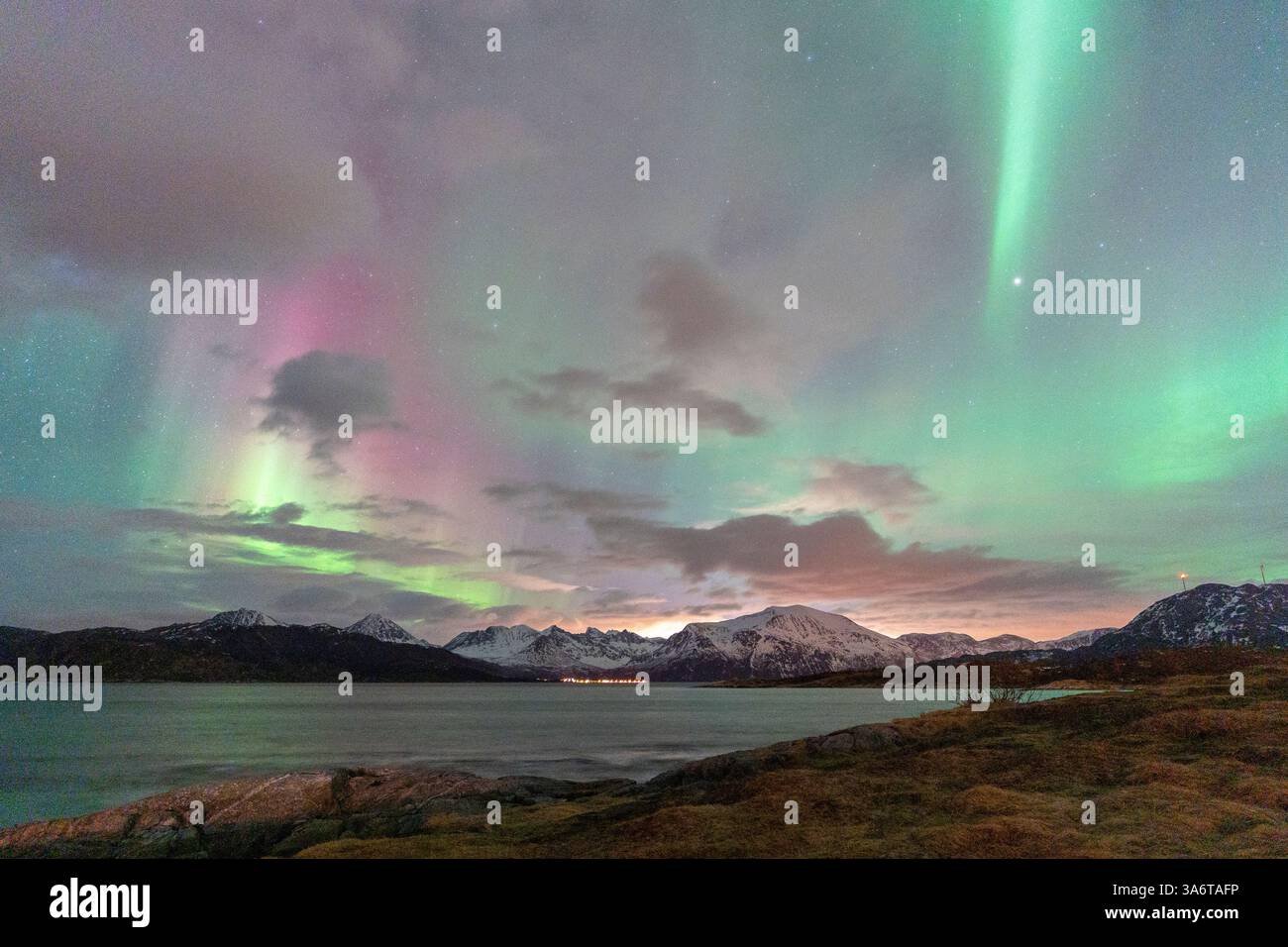 Wunderschöne Aurora Borealis über dem Haus auf der Insel Kvaløya, tanzende Nordlichter mit grünem Licht, roten und lila Strikes, klare farbige Strahlen Stockfoto