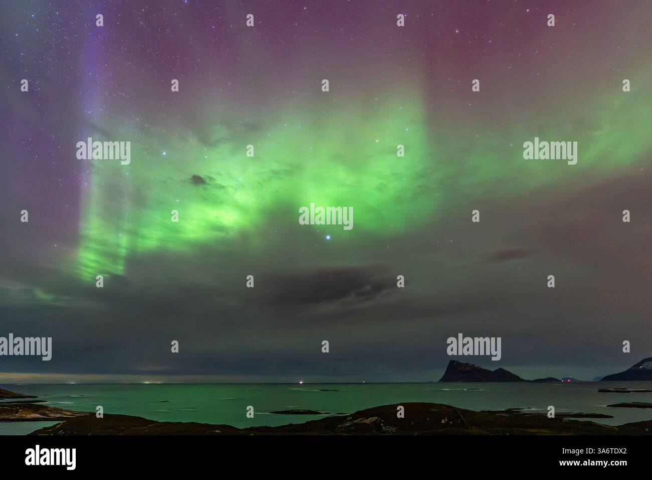 Wunderschöne Aurora Borealis über dem Haus auf der Insel Kvaløya, tanzende Nordlichter mit grünem Licht, roten und lila Strikes, klare farbige Strahlen Stockfoto