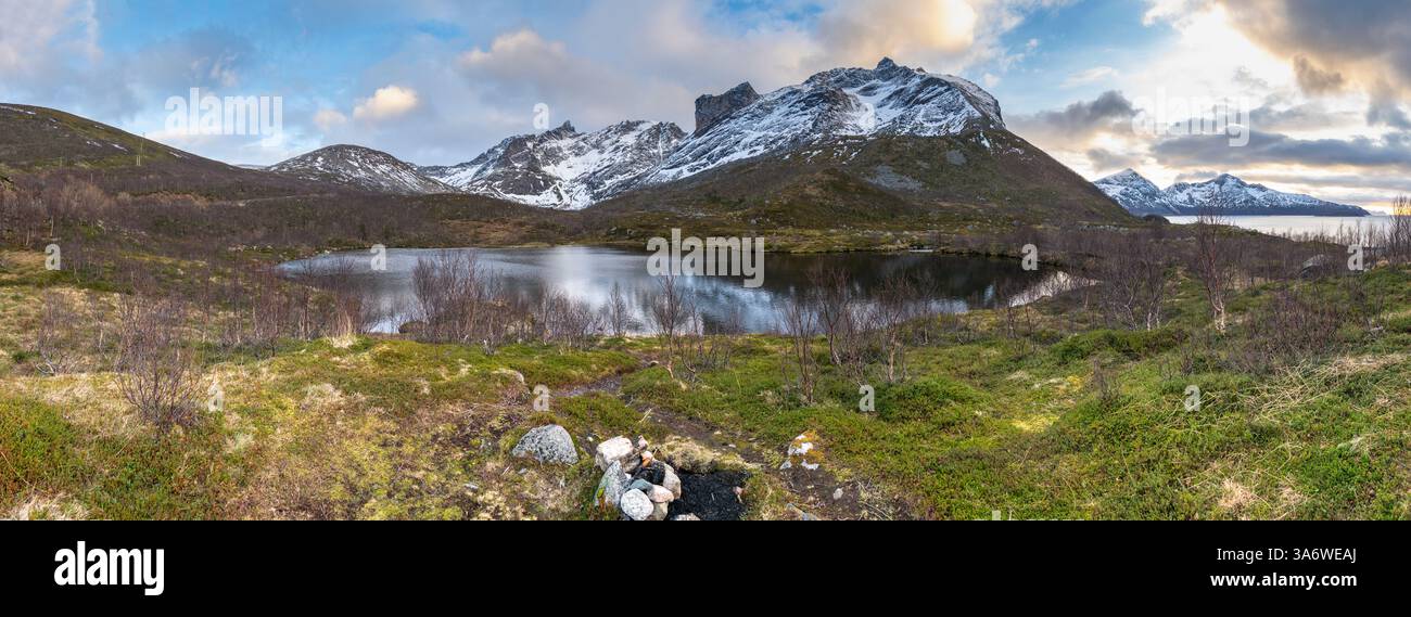 Panorama mit See und Strand des Nordatlantiks. Raue Natur auf den Inseln von Kvaløya, mit steilen felsigen Bergen. Kleine Birken und gelb Stockfoto
