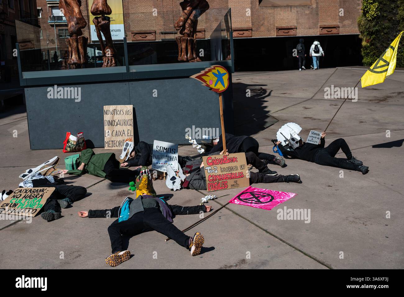 Madrid, Spanien. März 2025. Klimaaktivisten der Gruppe Extinction Rebellion, die Dinosauriermasken tragen, protestieren vor der Ausstellung Patagonischer Dinosaurier auf dem CaixaForum, um anzuprangern, dass die CaixaBank-Gruppe ihre Investitionen in die fossile Brennstoffindustrie weiter erhöht. Der Protest findet zeitgleich mit dem Weltklimatag statt. Quelle: Marcos del Mazo/Alamy Live News Stockfoto