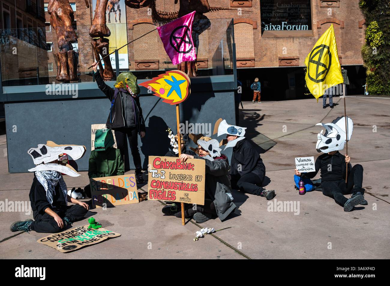 Madrid, Spanien. März 2025. Klimaaktivisten der Gruppe Extinction Rebellion, die Dinosauriermasken tragen, protestieren vor der Ausstellung Patagonischer Dinosaurier auf dem CaixaForum, um anzuprangern, dass die CaixaBank-Gruppe ihre Investitionen in die fossile Brennstoffindustrie weiter erhöht. Der Protest findet zeitgleich mit dem Weltklimatag statt. Quelle: Marcos del Mazo/Alamy Live News Stockfoto