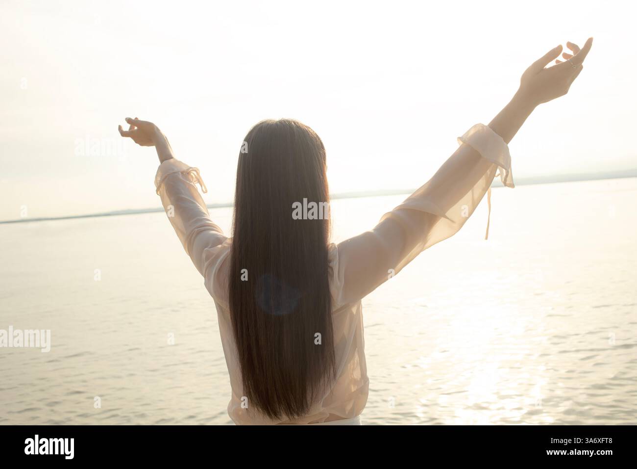 Die Figur einer freien Frau, die im Sonnenlicht eingetaucht ist, mit erhobenen Armen Stockfoto