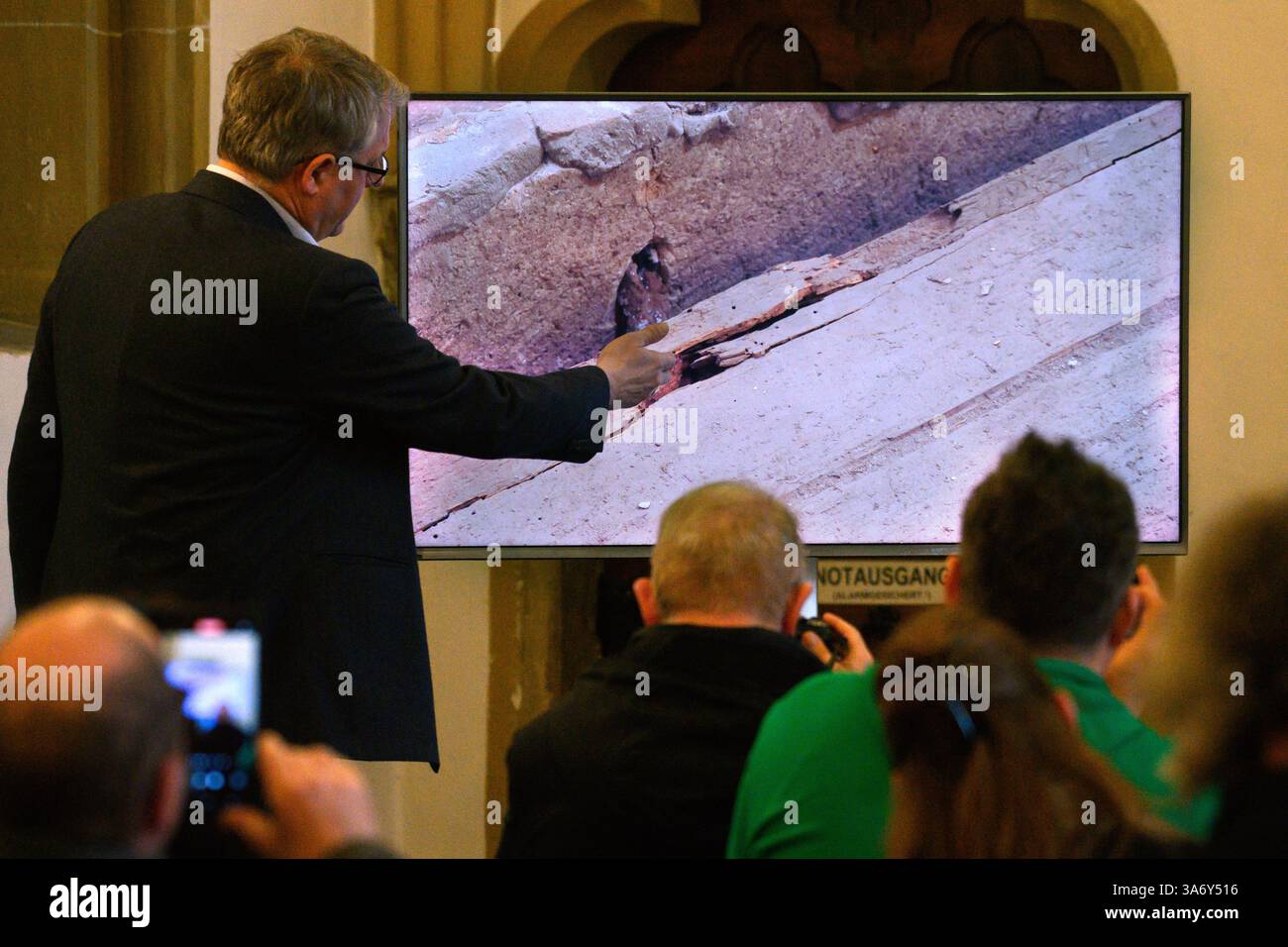 26. März 2025, Sachsen-Anhalt, Magdeburg: In der Sakristei des Magdeburger Doms erklärt Donat Wehner (l) vom Landesamt für Denkmalpflege und Archäologie Sachsen-Anhalt Medienvertretern die Beschädigung der Holzkiste im offenen Sarkophag mit Hilfe einer Live-Videoübertragung aus dem Gehege rund um das Grab Ottos des Großen. Seit Januar führen das Landesamt für Denkmalpflege und Archäologie und die Kulturstiftung Sachsen-Anhalt Untersuchungen zur Erhaltung des Denkmals durch. Bisherige Ergebnisse und weitere geplante Ergebnisse Stockfoto