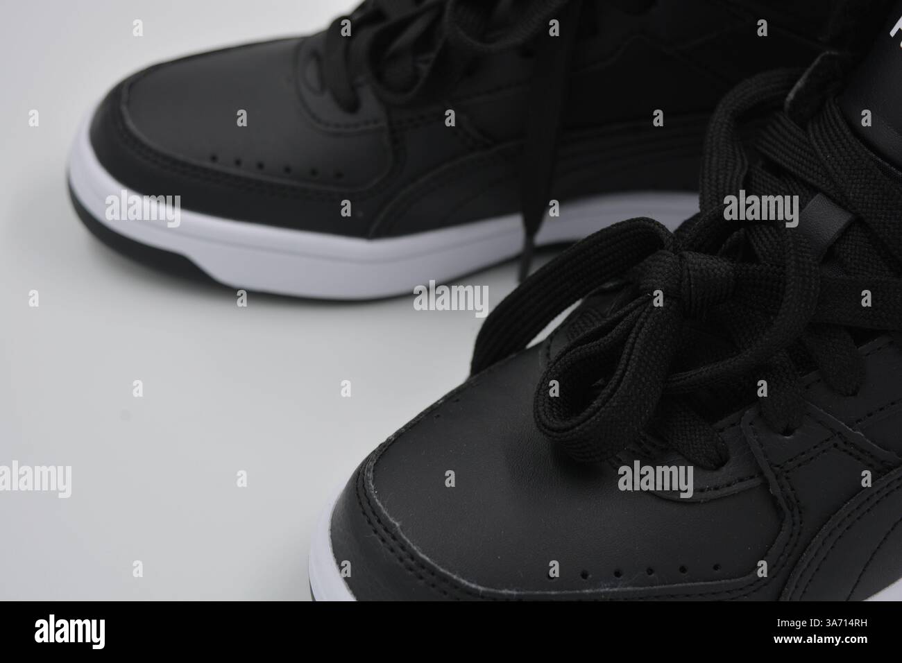 Schöne, junge Sportschuhe, schwarze Stiefel mit weißen harten Sohlen sind auf einem weißen plasti.. Warme Halbstiefel aus Leder mit Isolierung. Stockfoto