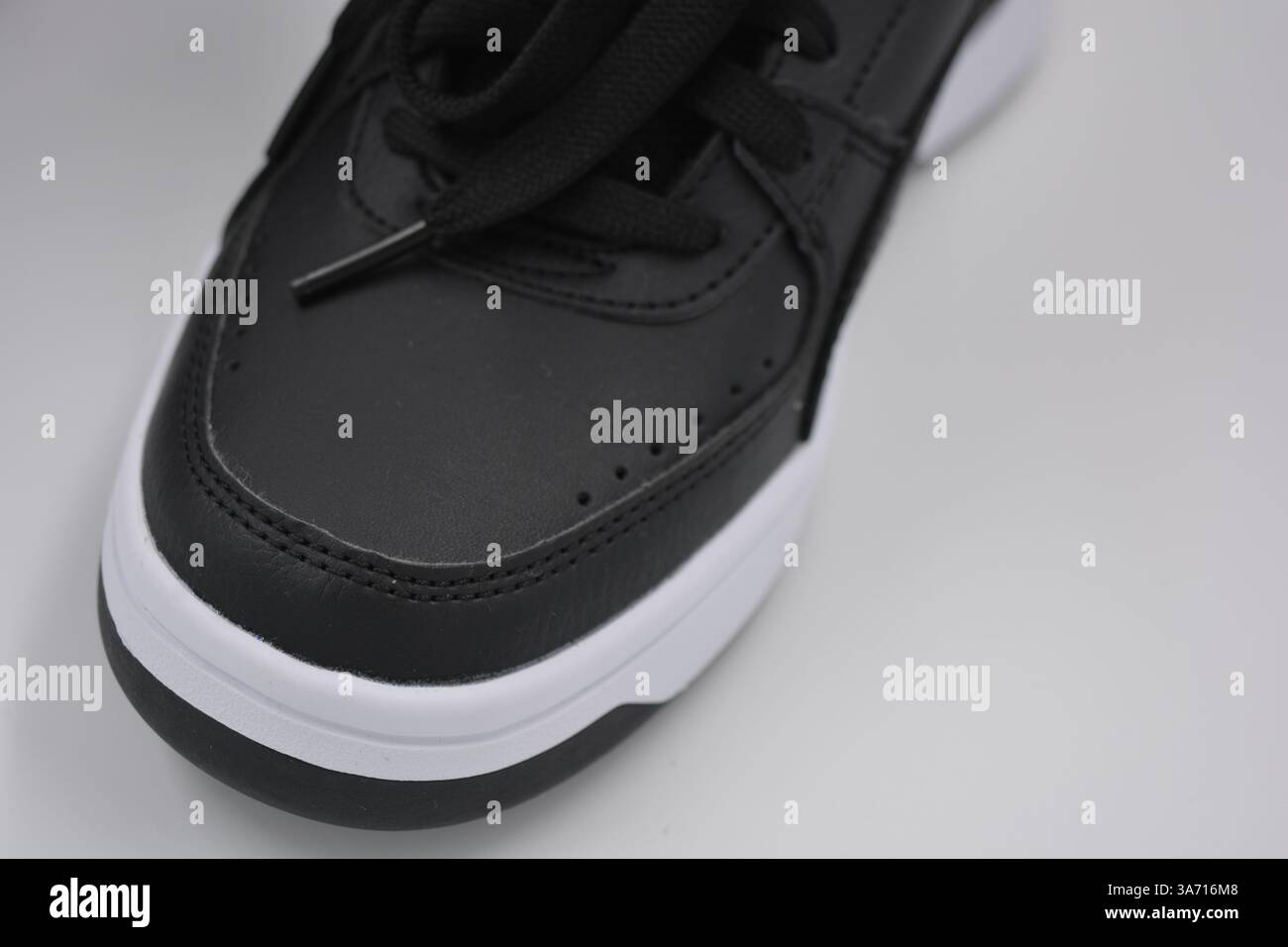 Schöne, junge Sportschuhe, schwarze Stiefel mit weißen harten Sohlen sind auf einem weißen plasti.. Warme Halbstiefel aus Leder mit Isolierung. Stockfoto