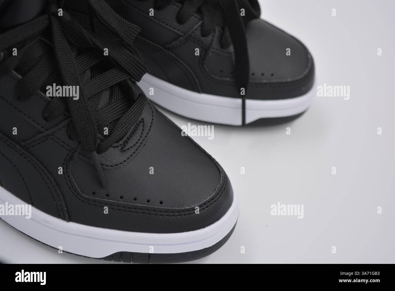 Schöne, junge Sportschuhe, schwarze Stiefel mit weißen harten Sohlen sind auf einem weißen plasti.. Warme Halbstiefel aus Leder mit Isolierung. Stockfoto