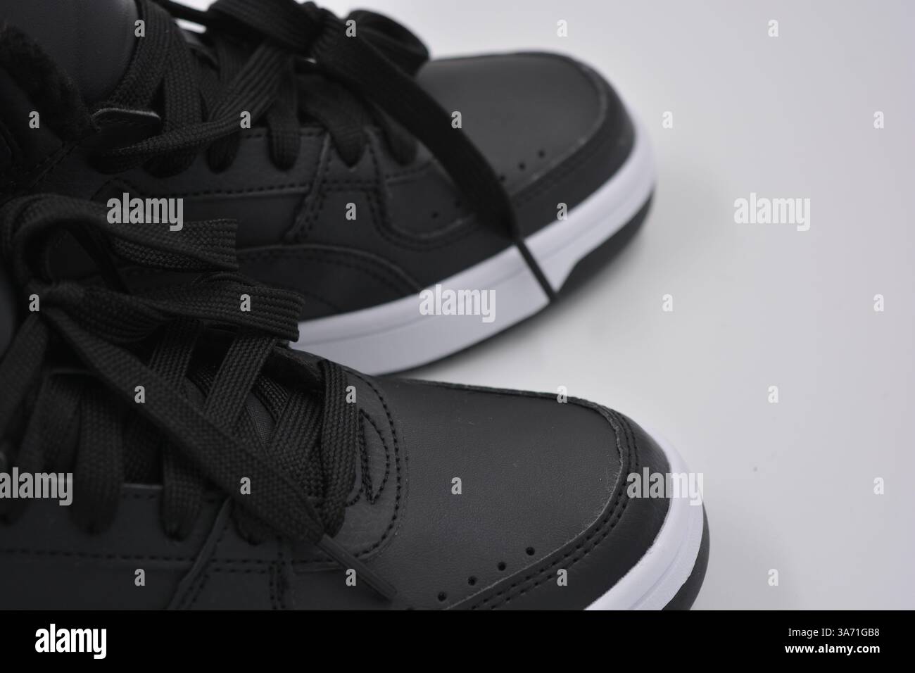 Schöne, junge Sportschuhe, schwarze Stiefel mit weißen harten Sohlen sind auf einem weißen plasti.. Warme Halbstiefel aus Leder mit Isolierung. Stockfoto