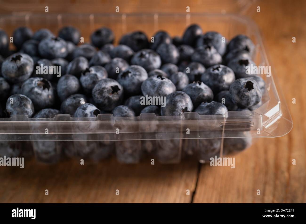 Heidelbeeren im Kunststoffbehälter auf Holztisch Stockfoto
