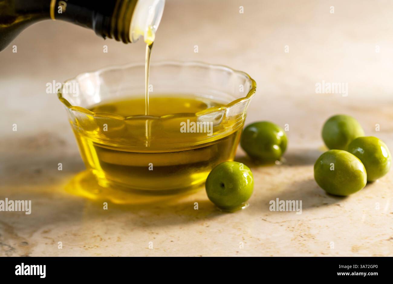 Olivenöl in eine kleine Glasschale mit Oliven auf dem Tisch gießen Stockfoto