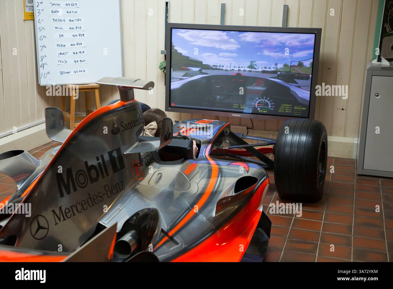 Ein kleines Mädchen im Rennwagen-Simulator ermöglicht es Besuchern, in einem MCLAREN MP4-21 F1-Showcar zu sitzen und zu fahren, um die alte Brooklands-Rennstrecke auf einem Bildschirm des Brooklands-Museums in Surrey zu erkunden. UK. (139) Stockfoto