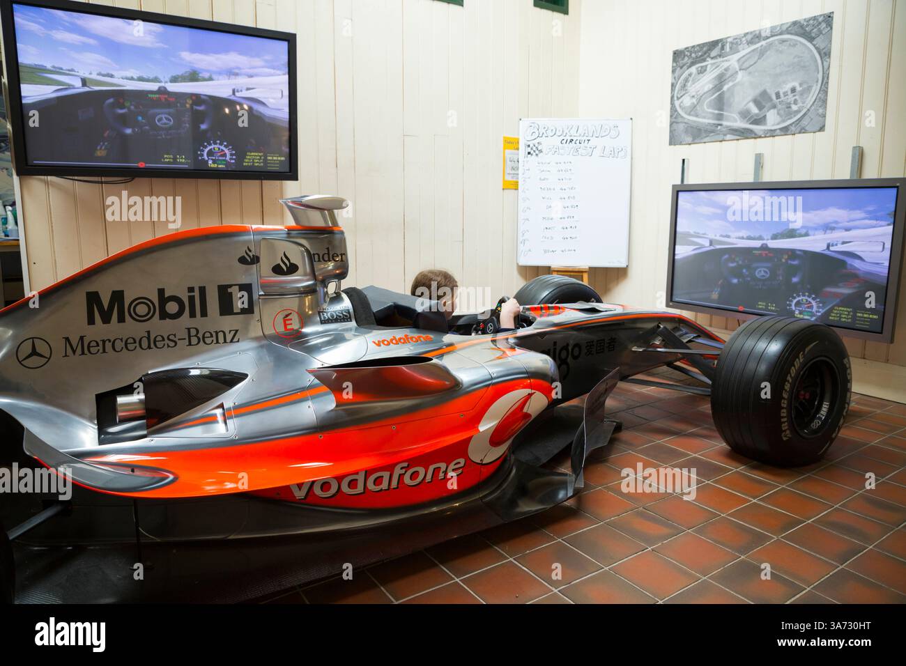 Ein kleines Mädchen im Rennwagen-Simulator ermöglicht es Besuchern, in einem MCLAREN MP4-21 F1-Showcar zu sitzen und zu fahren, um die alte Brooklands-Rennstrecke auf einem Bildschirm des Brooklands-Museums in Surrey zu erkunden. UK. (139) Stockfoto