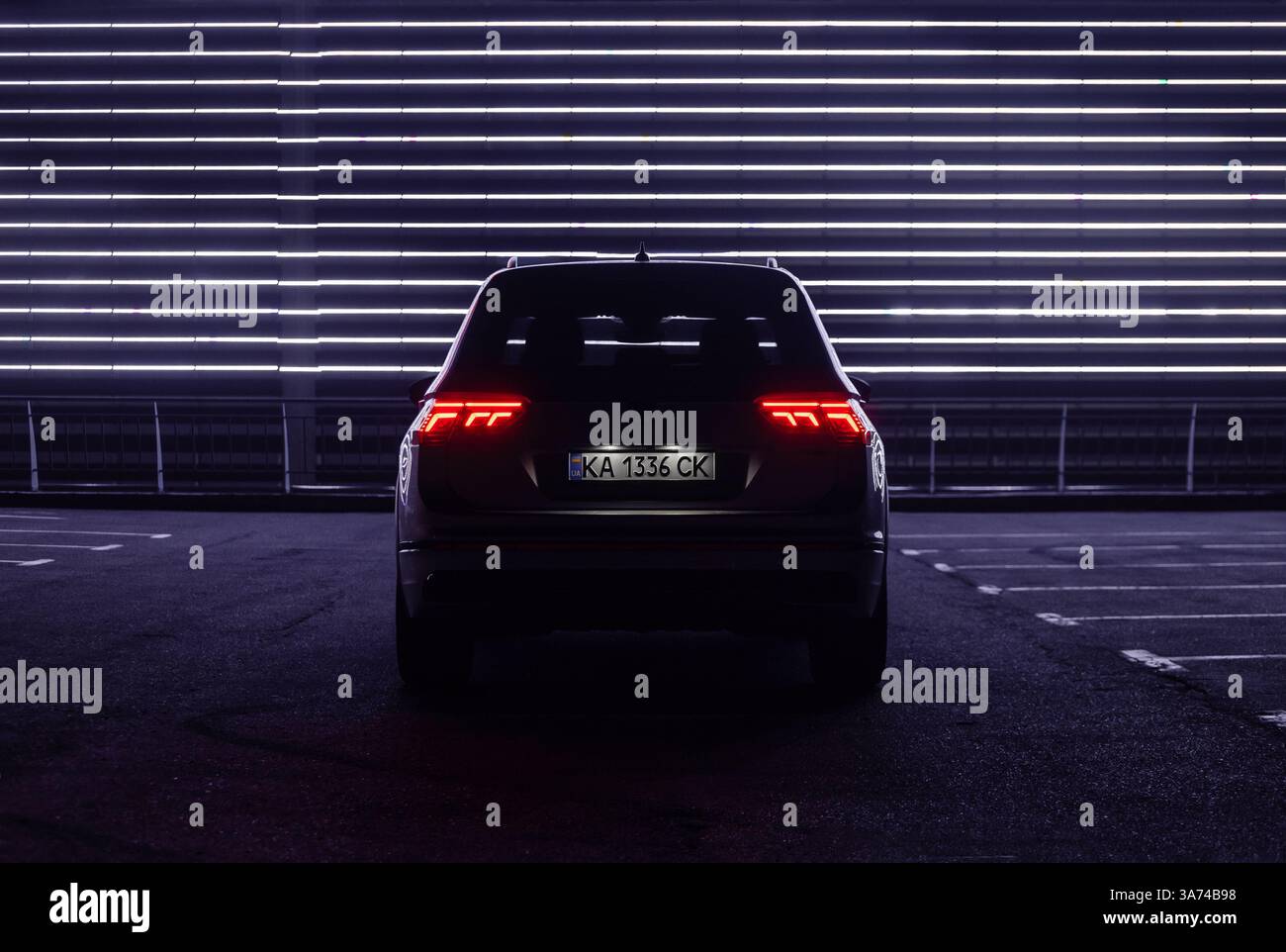 Volkswagen Tiguan in der dunklen Stadtstraße bei Nacht - dunkle Silhouette. Rückansicht des modernen SUV bei Nacht, violette Neonlinien im Hintergrund. Stockfoto
