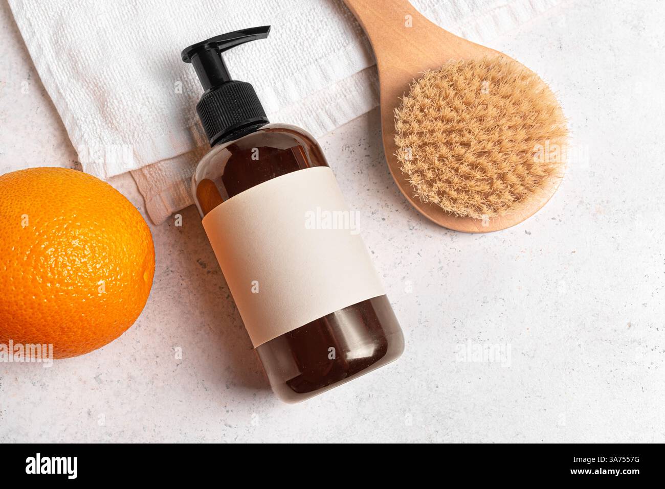 Spender für Körperpflegemittel, Holzbürste für Anti-Cellulite-Trockenmassage und Orangenfrucht flach auf weißem Handtuch. Anti-Cellulite, Körperpflege, d Stockfoto